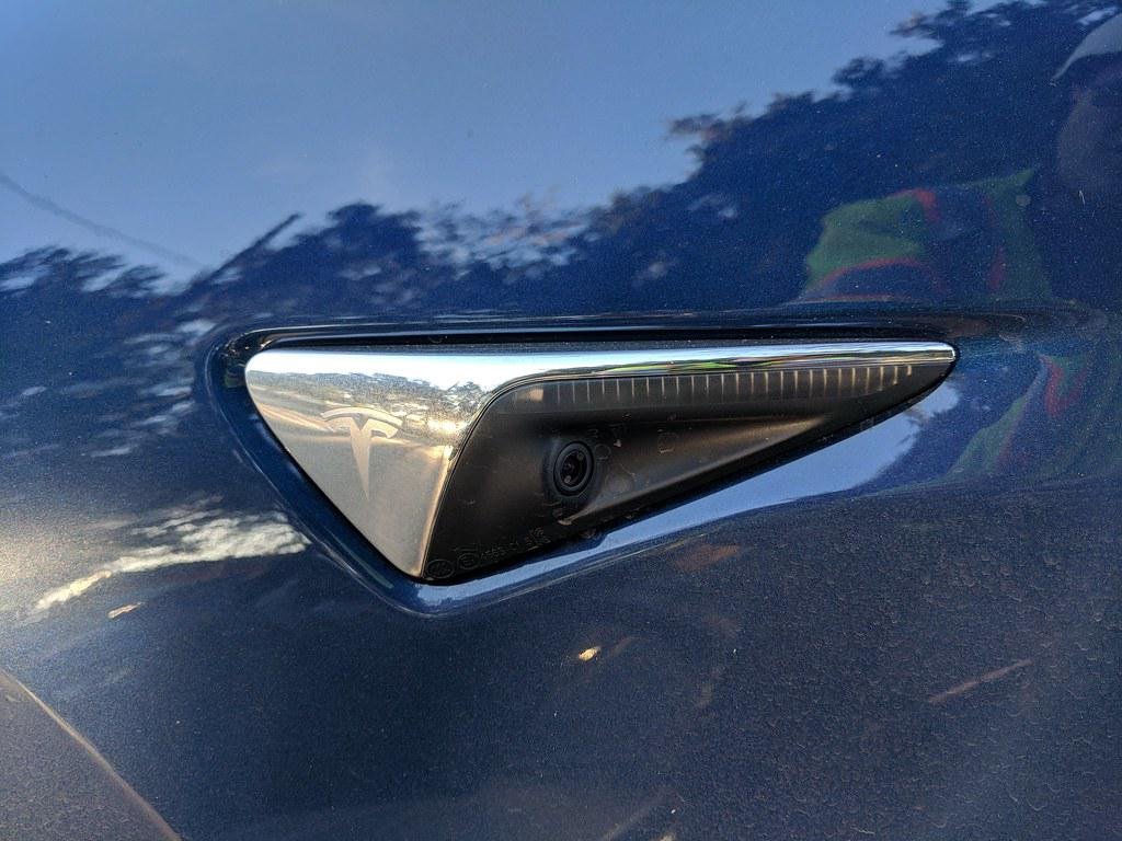 Close-up view of a Tesla car's exterior, showcasing its array of sensors, cameras, and radar units that power the Autopilot system.